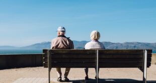 man and woman sitting on bench facing sea